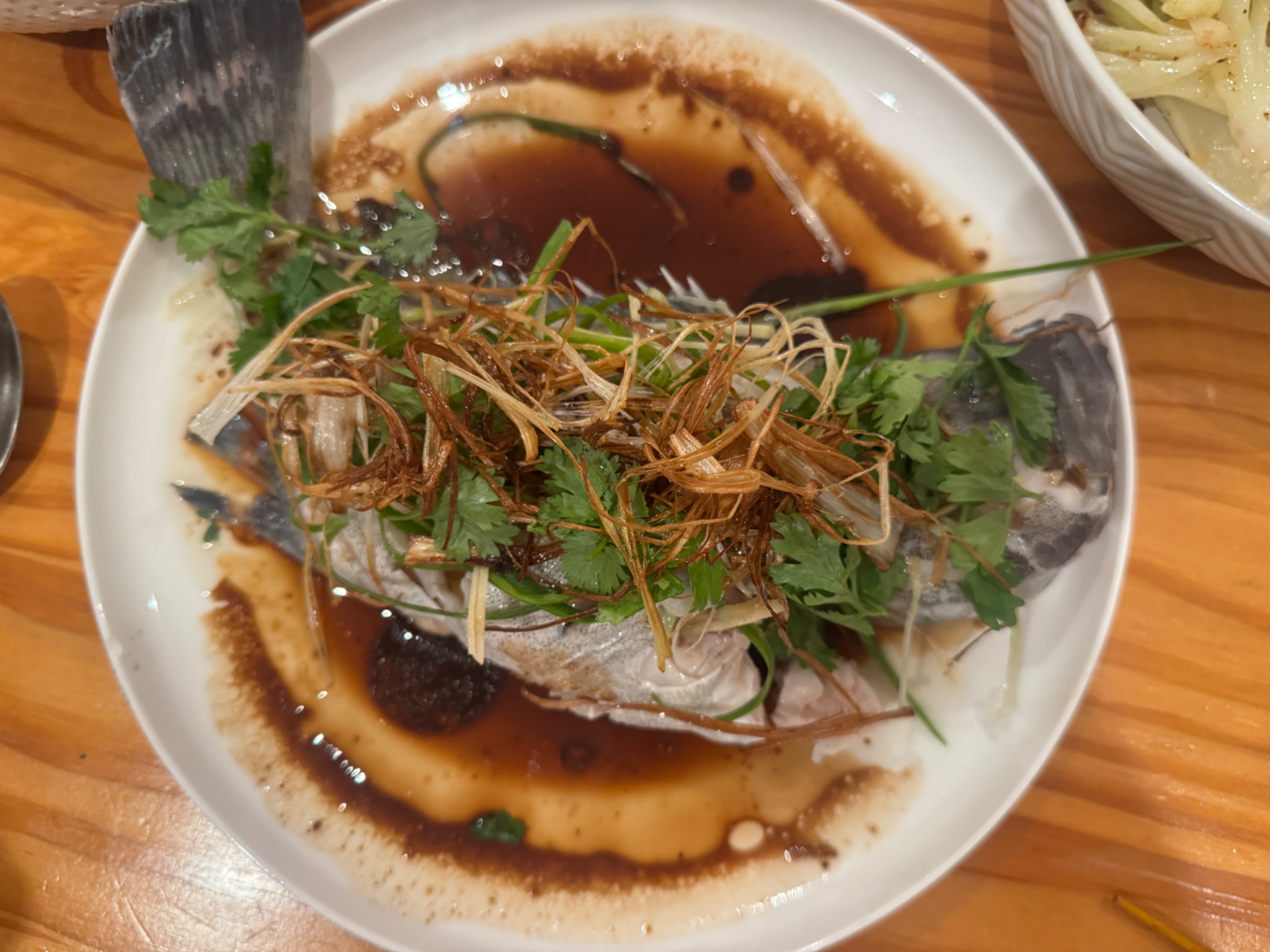 Finished Cantonese steamed grouper topped with crispy fried leek, scallion and coriander, soy pooled around the plate