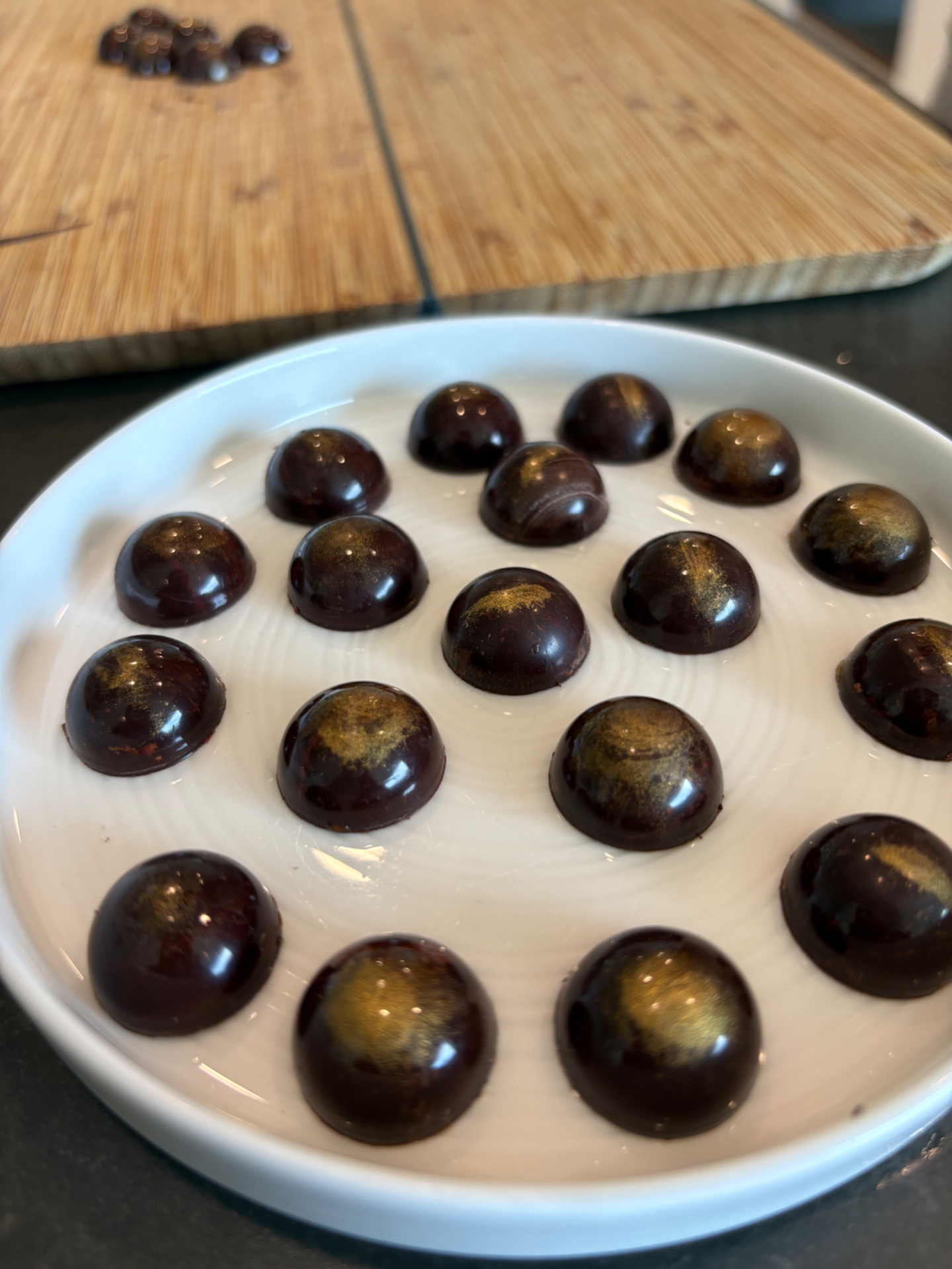 Finished dark chocolate bonbons, domed and high-gloss with a bronze lustre sheen, arranged on a white plate